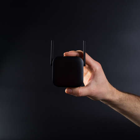 Hand connecting black wifi amplifier to electrical outlet, on black background.の写真素材