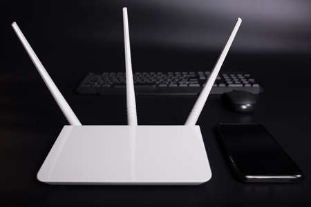 White wifi router with three antennas with smartphone and PC keyboard on black background.の写真素材