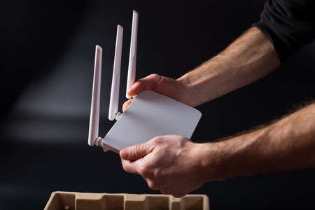 Man's hands holding new wifi router on black background. Unpacking new white router.の写真素材