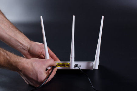 Hands connecting cable to white wifi router with three antennas.on black background.