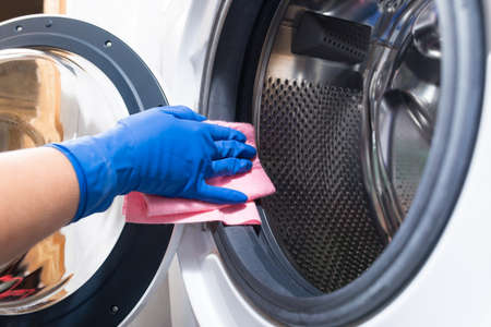 Hand in blue glovesw cleaning washing mashine with piece of clothの写真素材