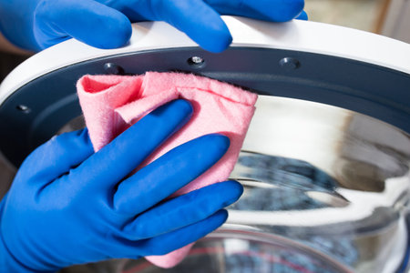 Hands in blue gloves close up, cleaning washing machine after using.
