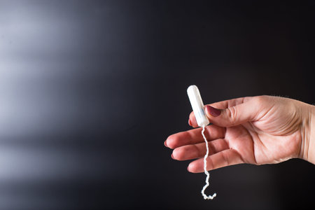 Female hand holding tampon close up, on black background.