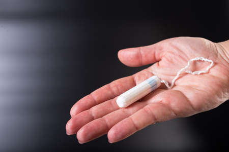 Tampon on woman hand close up, on black background with copy space.の写真素材