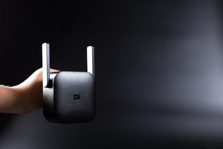 Black Xiaomi Pro WiFi Amplifier in hand, on black background, with copy space.