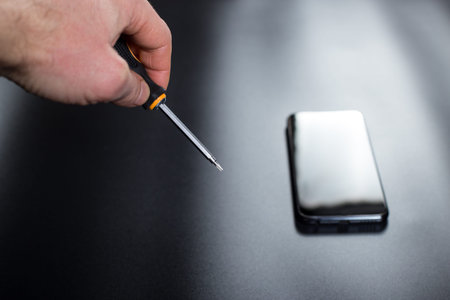 Hand with little screwdriver for smartphone repair and smartphone on black background.