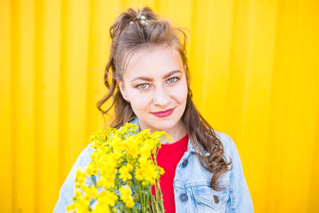 Portrait of young beautiful stylish girl with bouquet of yellow wild flowers.の写真素材