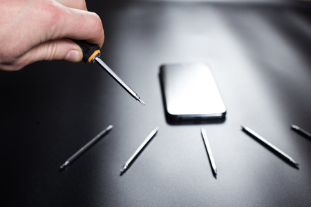 Man's hand holding small screwdriver for fixinf phone and set od tools for reparing elecrtonics on black background.の写真素材