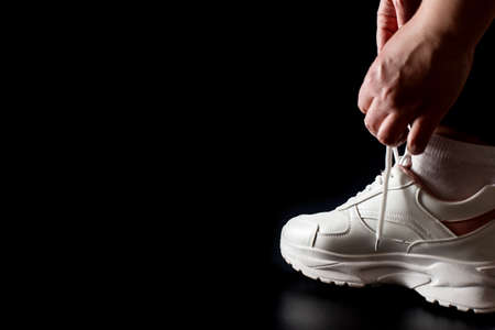 Putting on sport sneakers isolated on black with copy space. Tying shoelaces on white sneakers.の写真素材
