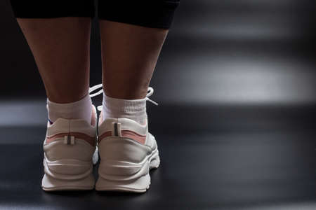 Feets of young fat girl in white sneakers close up, on black background.の写真素材