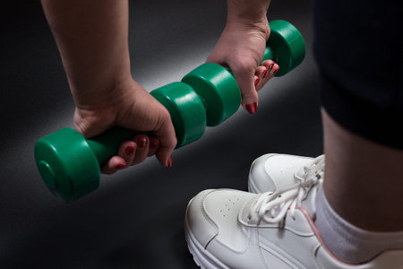 Fat young girl warming up with dumbbells with white sneakers on feet. close up on black background.の写真素材