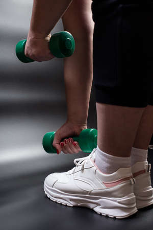 Fat young woman training with dumbbells in gym, on black background.の写真素材