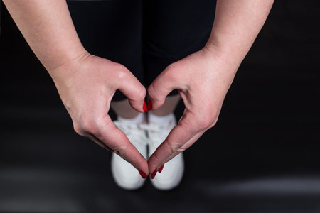 Girl's hands showing heart shape for her sneakers in the gym, on black background.