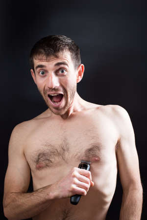 Scared man with opened mouth and funny face, fist ime shaving his chest on black background.の写真素材