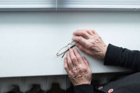 Elderly people suffering from loneliness. An elderly woman's hands are holding glasses on the windowsill.の写真素材