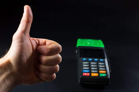 Thunb up for paying contactless terminal on black background.