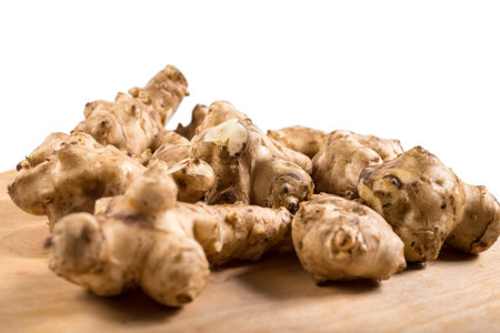 Tubers of Jerusalem artichokes close up on a wooden table, on a white background.