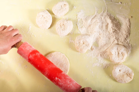 Use a rolling pin to roll out the dough for pies on the table with flour.