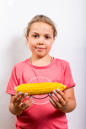 A tanned school-age girl holding a swing of corn on a white background.