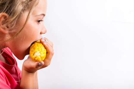 Hungry girl eating sweet corn on a white background with copy space.の写真素材