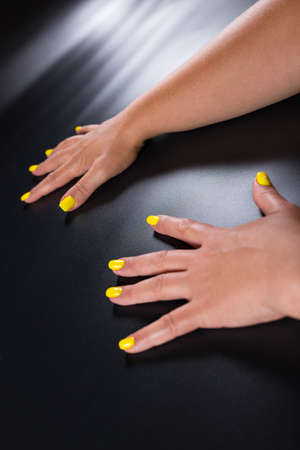 Tanned female hands with yellow manicure, on black background.の写真素材