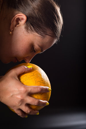 Face of yung woman smells yellow ripe melon in hands, on black background.の写真素材