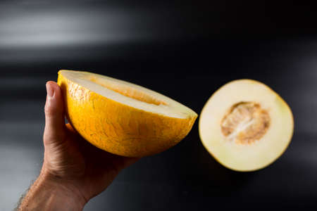 Two halves of yellow melon in male hand, on black background.の写真素材