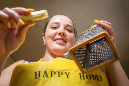 Young beautiful house wife wear apron and holding grater with cheese, smiling to the camera.の写真素材