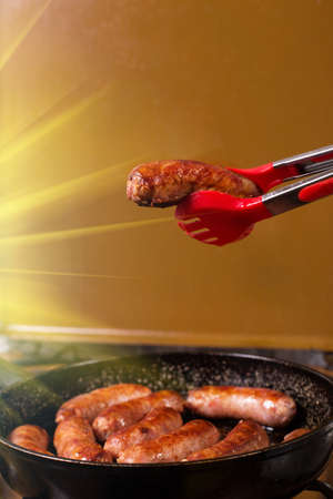 Picking ready fiede sausage from a frying pan with kitchen squidson a kitchen stove background.の写真素材