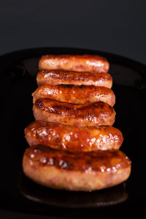 Fried sausages, close up on black plateand on black background.