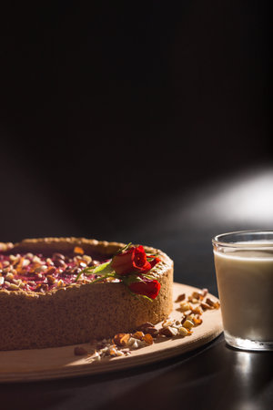 Cheese cake with peanuts on wooden plate and with fllowers on it and glass of milk, on black background.の写真素材