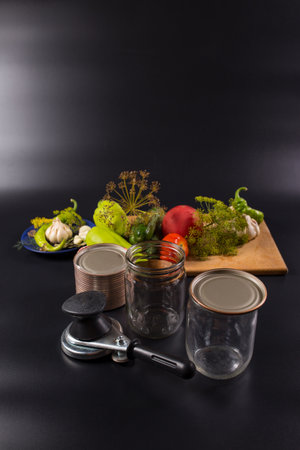 Glass jars for preservation with canning tool and prepared vegetables and herbs on black background.の写真素材