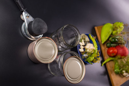 Glass jars with caning tool prepared close to vegetables for preservation, on black background.の写真素材