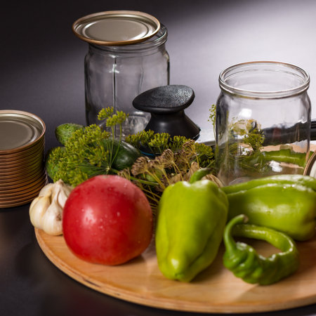 Canning vegetables in glass jars with canning tool on wooden board, on black background.の写真素材