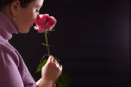 Sensual young girl inhales the delicate scent of a pink rose, on black background.の写真素材