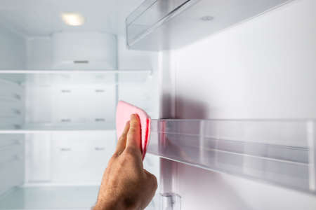 Hand cleaning empty fridge inside with piece of cloth.の写真素材