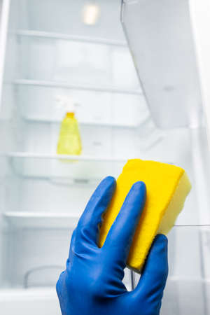 Hands in blue glove cleaning fridge inside with detergent sprtay from dust and badf odor.の写真素材