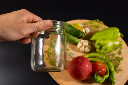 Hnd holding close clean glass jar and fresh vegetables blured on black background.