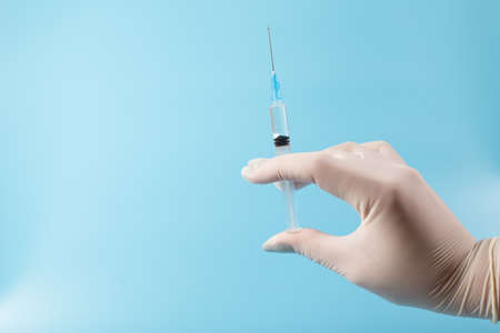 Doctor hands in white gloves holding syringe with vaccine, close up on blue background with copy sapce.の写真素材