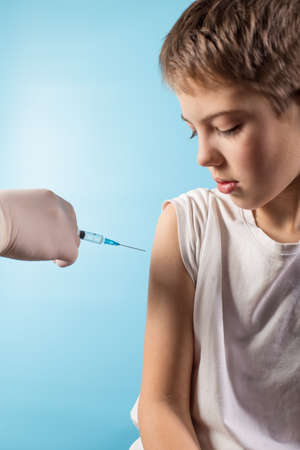 Doctor hand in sloves making vaccination for school boy, close up on blue background.の写真素材