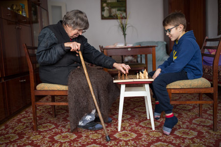 Little boy play chess with his grandmother, in grandma home, lifestyle background.