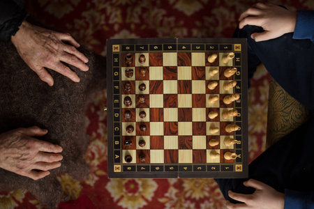 Top view chessboard and hands of old lady and young boy, close up at home lifestyle.