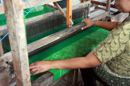 BALI, INDONESIA - AUGUST 26, 2011  An unidentified Balinese woman operates a manual weaving contraption to knit batik cloth, on August 26, 2011 in Bali, Indonesia  Batik-making is an important part of Indonesian culture   のeditorial素材