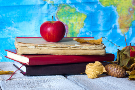 Back to school concept. Old vintage books and apple and autumn leaves over geografic map background