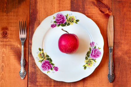 One ripe red apple on plate with fork and knife on wooden backgroundの写真素材