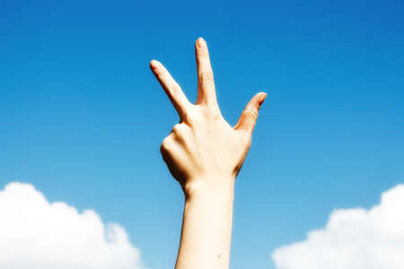 Three finger salute hand gesture, on blue sky backgroundの写真素材