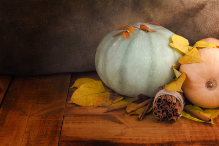 Autumn background with yellow maple leaves, pumpkins and cinnamon on aged wood with copy space. Mockup for seasonal offers and holiday post cardの写真素材