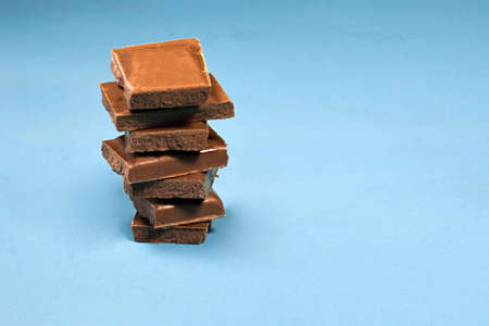 stack of chocolate pieces, close up shot with selected focus on a bright rustic wooden backgroundの写真素材