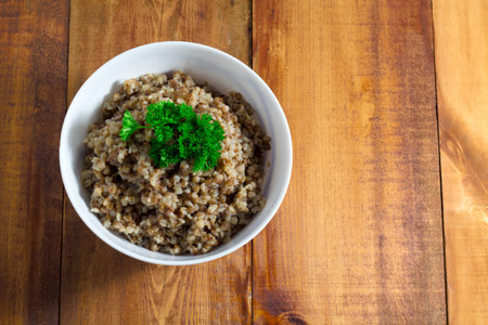 Buckwheat porridge in bowl with parsley on a wooden background closeup