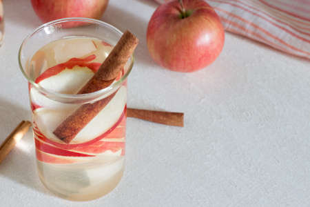 Glass with fresh apple water and cinnamon sticks on light tableの写真素材